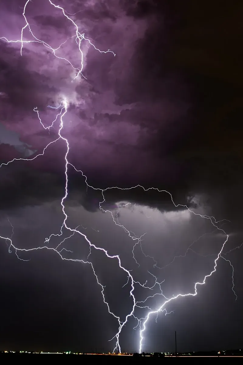Bright white lightning bolts striking from dark purple storm clouds at night