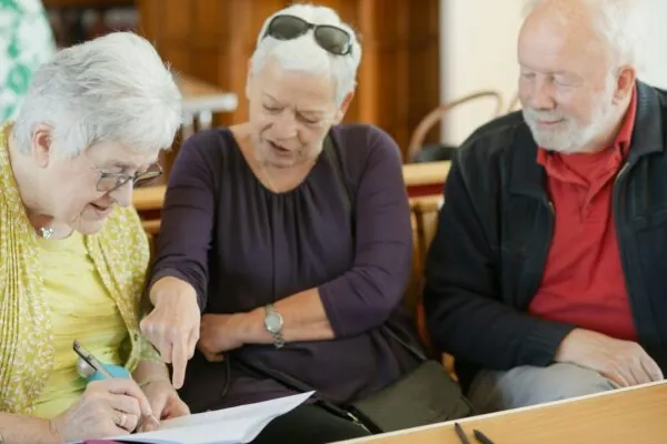 Three older adults are looking at a paper